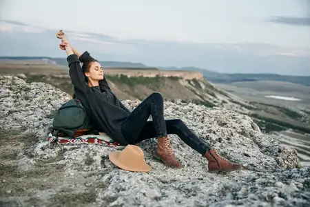 Уверенная в себе женщина покоряет вершину с рюкзаком за плечами, подняв руки вверх в знак триумфа