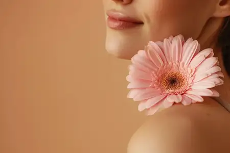На изображении запечатлена красота женщины с нежной улыбкой, которую подчеркивает ярко-розовый цветок, создавая свежий образ