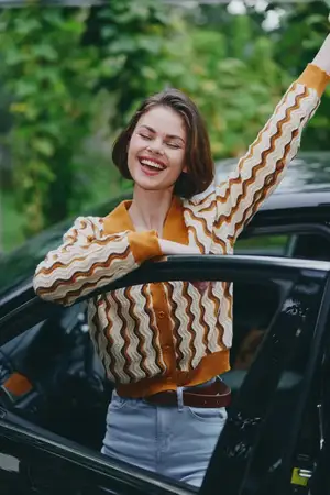 Автомобиль, водитель, женщина, улыбка: радостная женщина наслаждается моментом у двери автомобиля, поднятые руки и широкая улыбка выражают уверенность, энтузиазм и готовность к новым приключениям