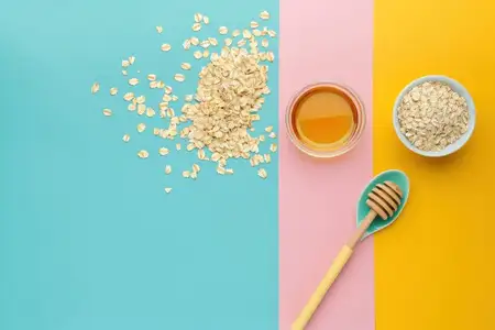 Овес, рассыпанный рядом с миской овса и меда на красочных пастельных фонах синего, розового и желтого цветов