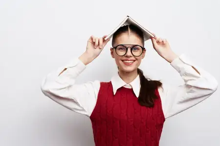 Счастливая молодая девушка балансирует книгой на голове с жизнерадостным выражением лица