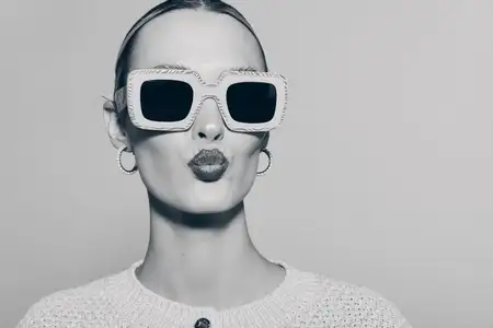Портрет бледной женщины европеоидной расы, посылающей воздушный поцелуй, в больших солнцезащитных очках и серьгах-кольцах