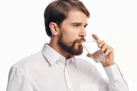 Красивый мужчина со стаканом воды на светлом фоне