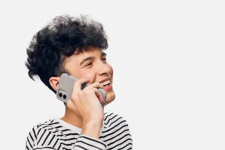 Улыбающийся мужчина с вьющимися волосами разговаривает по смартфону на белом фоне