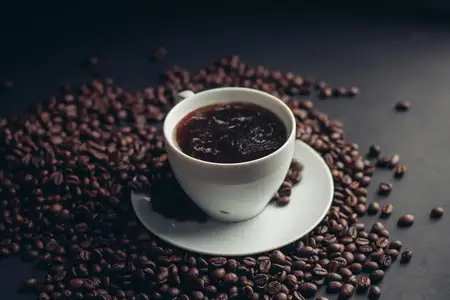 Кофейные зерна и чашка на белом блюдце на темном фоне
