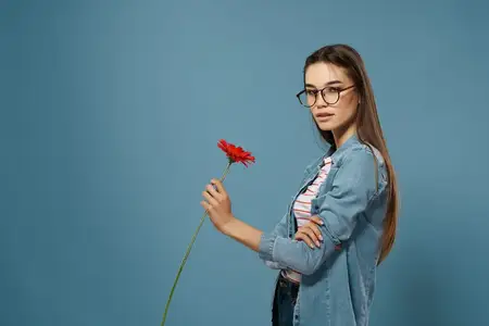 Симпатичная брюнетка с красным цветком позирует в атмосфере гламура, романтики и любви