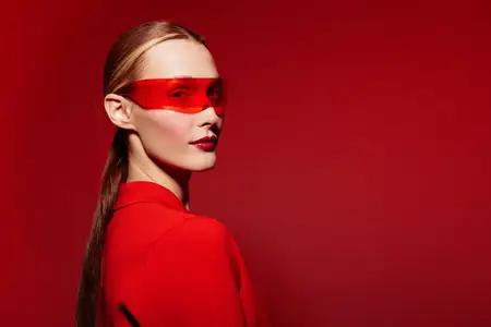 Модная женщина в красных солнцезащитных очках и красном наряде позирует на красном фоне