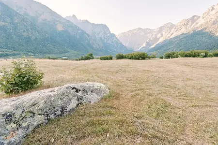 Луг в горной долине с большим камнем, бурой травой и низким кустарником