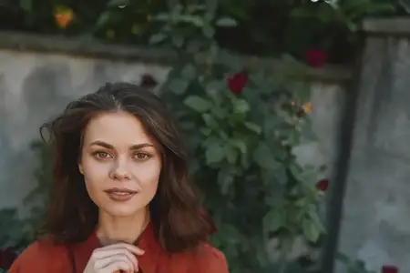 Искренний уличный портрет женщины в красном, демонстрирующий подлинное настроение, стойкость и повседневную красоту в мирной садовой обстановке