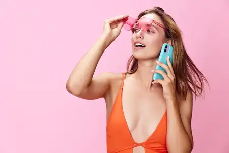 Женщина в ярком оранжевом купальнике делает селфи на свой мобильный телефон во время солнечного пляжного отдыха