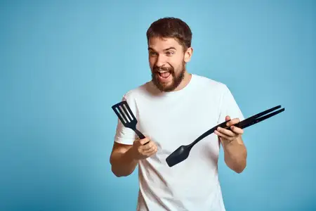 Мужчина в белой футболке готовит еду на кухне на синем фоне
