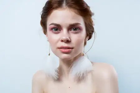Веселая женщина с обнаженными плечами, пушистыми серьгами, косметикой и украшениями