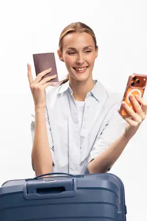 Молодая женщина с чемоданом, держащая паспорт и смартфон, делает селфи