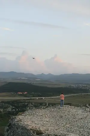 Человек стоит на вершине холма, любуясь воздушным змеем, парящим в небе во время неторопливого дня путешествия