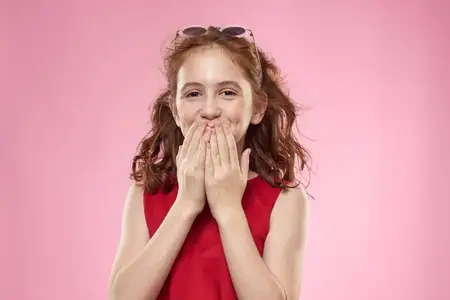 Весёлая маленькая девочка в тёмных очках и красном платье на розовом фоне