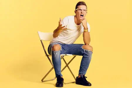 Симпатичный мужчина сидит на стуле в белой футболке и джинсах