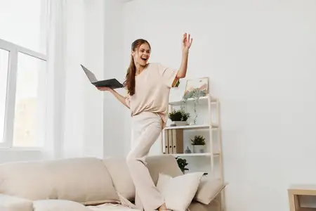 Улыбающаяся женщина работает за ноутбуком дома, наслаждаясь фрилансом в уютной гостиной
