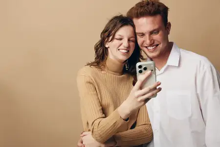Счастливая молодая пара в повседневной одежде обнимается и делает селфи на смартфон