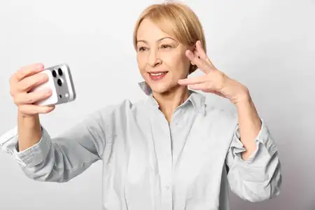 Пожилая женщина со светлыми волосами делает селфи на смартфон