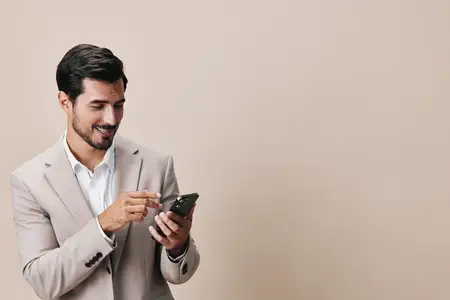 Молодой мужчина в деловом костюме улыбается, держа в руке смартфон