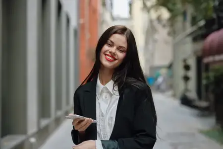 Деловая брюнетка с красными губами улыбается, показывая зубы, с телефоном в руках