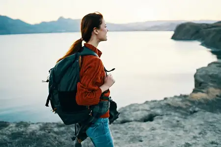 Женщина-туристка на закате у моря в горах, за спиной у неё рюкзак