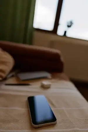 Изображение изображает уютный интерьер с теплым светом, смартфон на столе, мягкий диван на заднем плане и тихое, расслабленное настроение, подходящее для лайфстайл- или домашних проектов