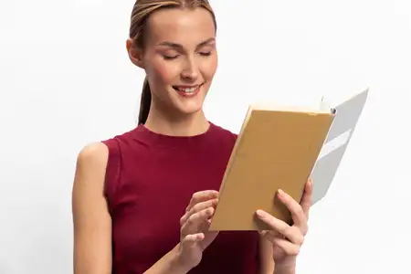 Улыбающаяся женщина держит и читает книгу в мягкой обложке, изолированная на белом фоне