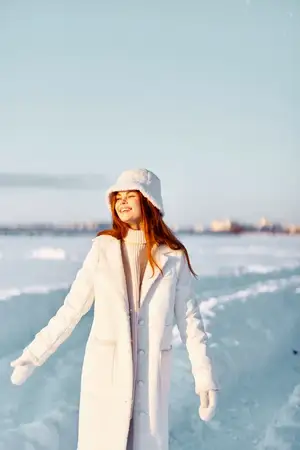 Женщина в белом пальто и шапке гуляет по зимнему пейзажу, вдыхая свежий воздух