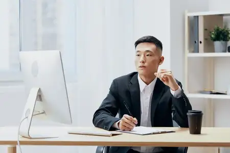 Азиатский мужчина работает за компьютером, рядом стоит чашка кофе