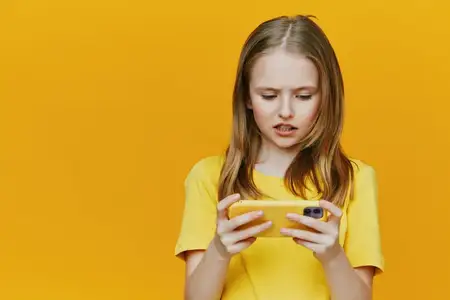 Юная девушка в ярко-желтой рубашке, удивленно смотрящая на смартфон