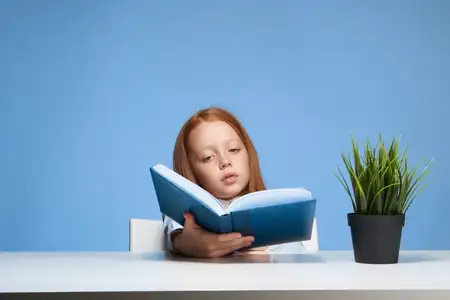 Школьница сидит за столом с книгой, погружённая в учёбу и детство