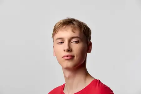 Студийный снимок молодого человека в ярко-красной футболке на однотонном фоне, передающий непринужденность, уравновешенность и современный стиль, подходящий для использования в маркетинге, интернете…