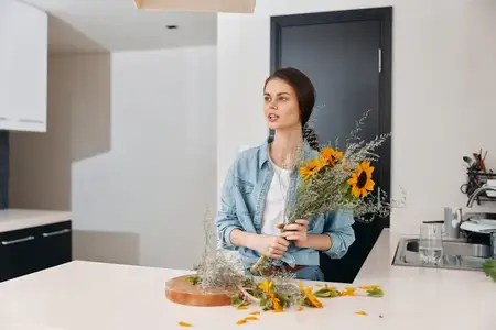 Симпатичная женщина-европейка стоит на зеленой кухне с букетом цветов: летний образ жизни молодой привлекательной девушки в стильном цветочном интерьере