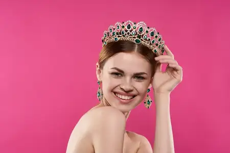 Привлекательная женщина с обнаженными плечами, в украшениях и с косметикой, позирует на изолированном фоне