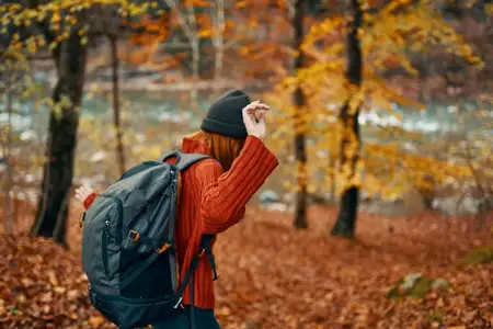 Женщина в свитере с рюкзаком отдыхает в парке у реки на природе осенью