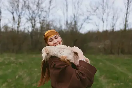 Ласковая сцена женщины и козлёнка на улице, повседневная одежда, деревенская обстановка, мягкий свет, непринуждённое настроение, повседневное счастье и связь с природой