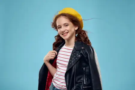 Модная девушка в черной куртке и желтой футболке в полоску с билетом на фоне голубого цвета