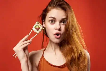 Эмоциональная женщина с палочками для еды и роллами суши в качестве закуски