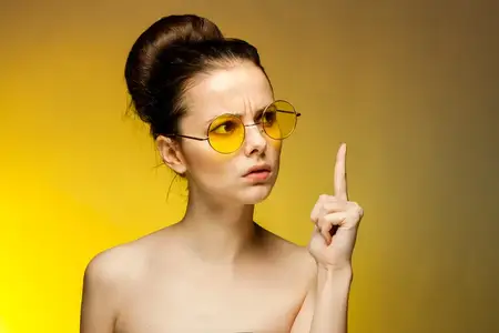 Симпатичная женщина в жёлтых очках с обнажёнными плечами жестикулирует руками, передавая эмоции
