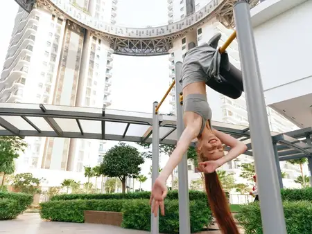 Женщина с длинными волосами висит вниз головой на турнике в современном тренажёрном зале под открытым небом