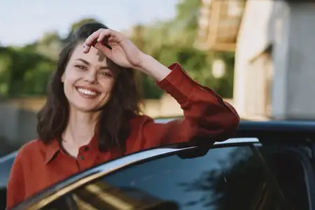 Непринужденная уличная сцена: веселая девушка опирается на автомобиль