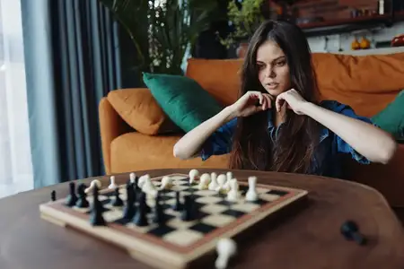 Женщина играет в шахматы дома, используя деревянную доску, установленную на столе в гостиной