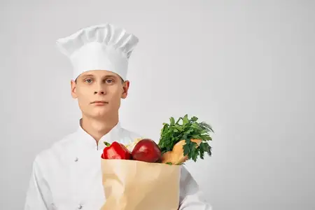 Мужчина в поварской форме с пакетом продуктов работает на кухне ресторана