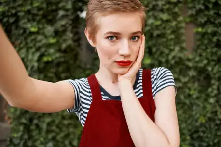 Улыбающаяся короткостриженая женщина с красными губами, крупным планом на открытом воздухе