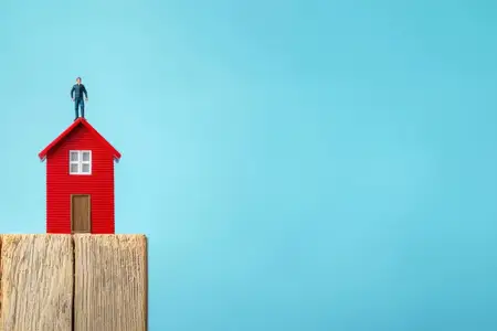 Символическое изображение успеха в домовладении: на этом снимке миниатюрная фигурка стоит на маленьком красном домике на ярко-голубом фоне, отражая стабильность и достижение