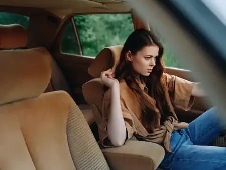 Задумчивая молодая женщина в винтажном автомобиле, одетая в повседневную одежду, излучает естественные эмоции в окружении безмятежной зеленой среды