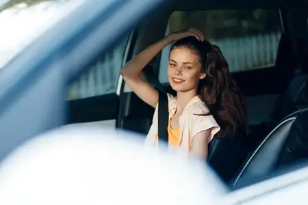 Молодая женщина с длинными волнистыми волосами улыбается, сидя в автомобиле, демонстрируя радостное выражение лица