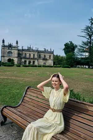 Портрет женщины, сидящей на скамейке в парке у замковой архитектуры, платье, улыбка, на свежем воздухе, демонстрирующий аутентичность и инклюзивность