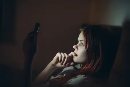 Женщина с телефоном в руках лежит в постели ночью перед сном